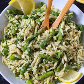 Lemon asparagus orzo in a white serving bowl with wooden spoons and lemon slices