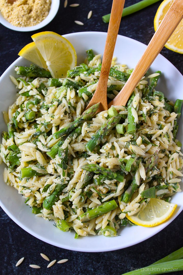 Lemon asparagus orzo in a white serving bowl with wooden spoons and lemon slices