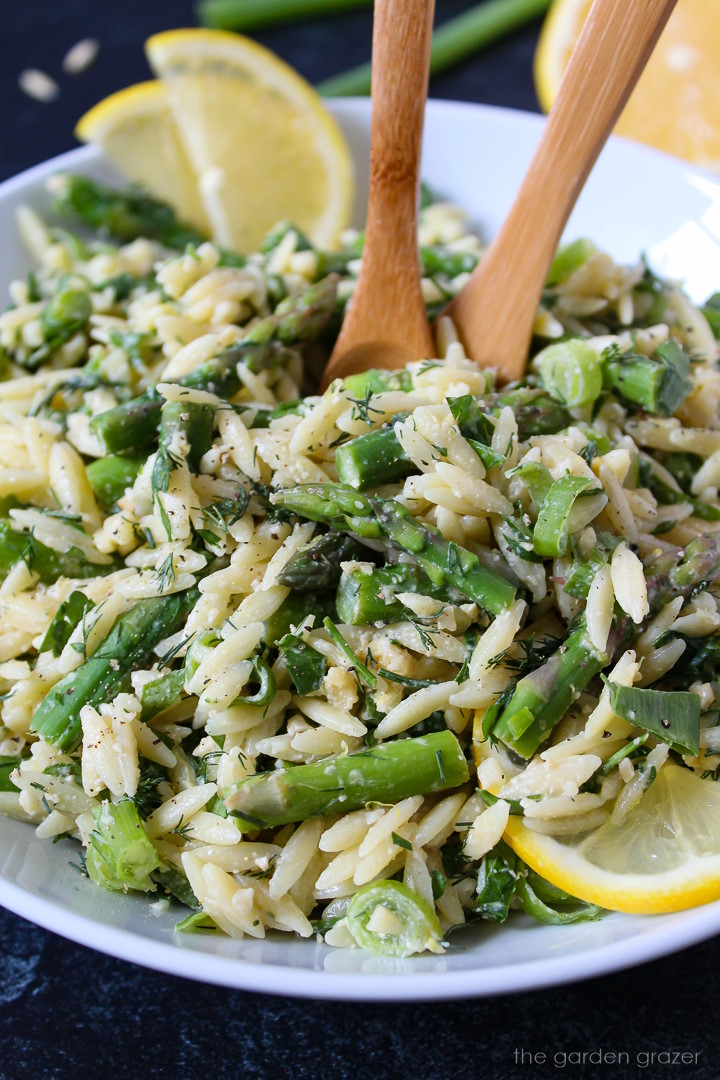 Close up view of lemon asparagus orzo in a white serving bowl with wooden spoons