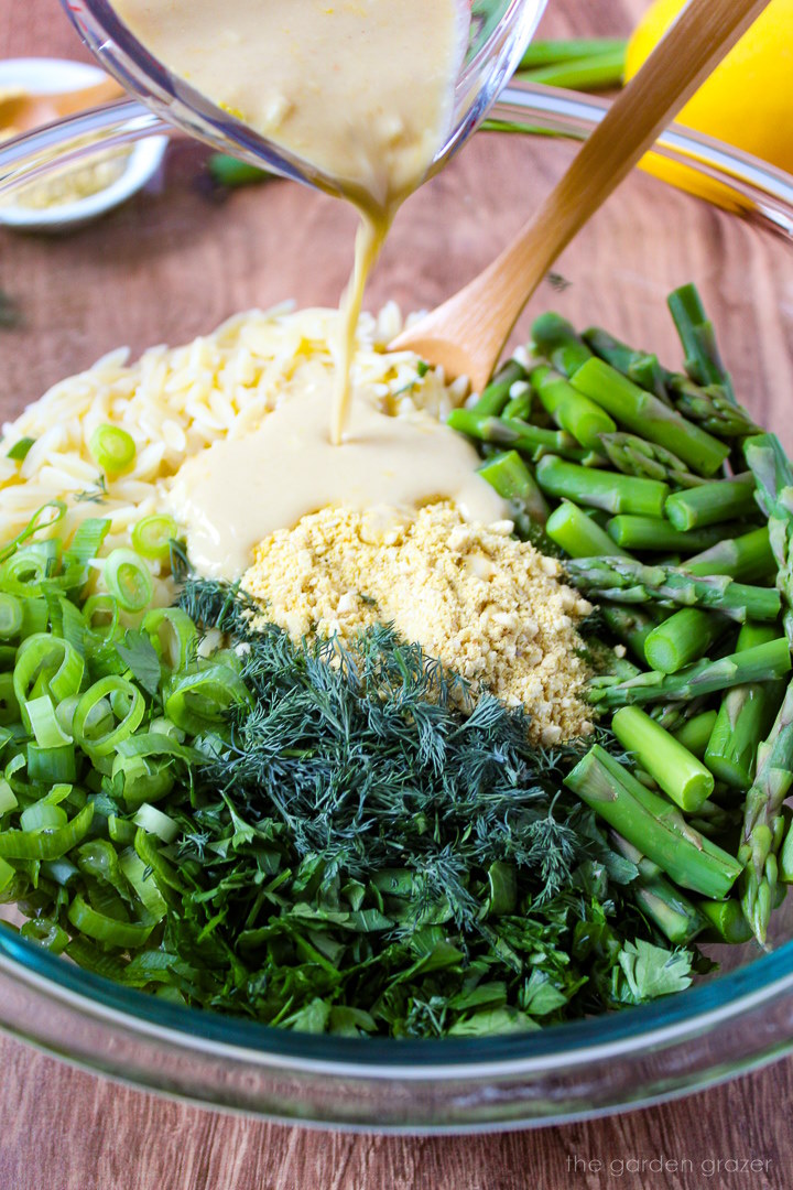 Lemon tahini dressing being poured over prepared ingredients in a glass mixing bowl