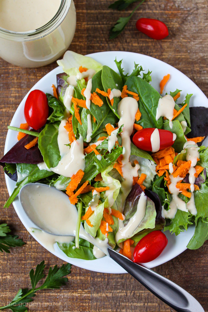 A fresh mixed greens salad on a white plate with carrot and tomato