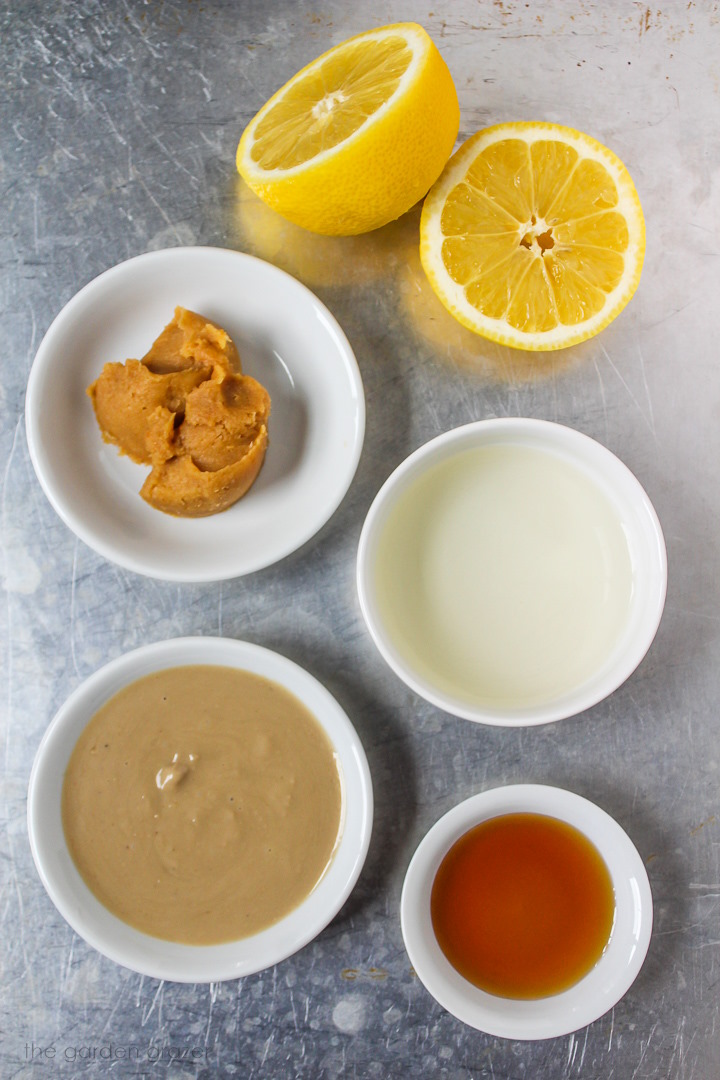 Fresh lemon, white miso, rice vinegar, tahini, and maple syrup ingredients laid out in bowls on a metal tray