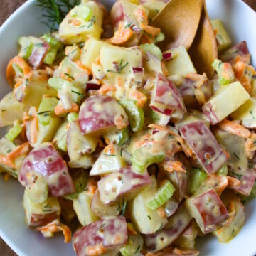 Vegan potato salad with fresh dill in a white serving bowl with bamboo spoons
