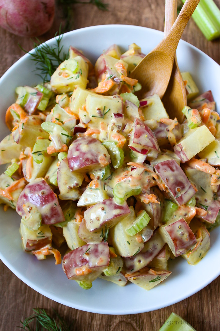 Vegan potato salad with fresh dill in a white serving bowl with bamboo spoons