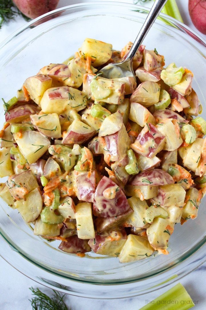 Overhead view of vegan potato salad mixed with a creamy dressing in a large glass bowl