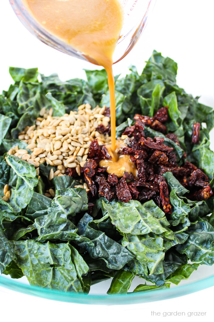 Prepared dressing being poured over chopped kale in a large glass bowl