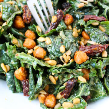 Close up view of a fork piercing kale and roasted chickpea salad on a white plate