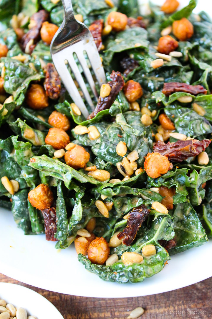 Close up view of a fork piercing kale and roasted chickpea salad on a white plate