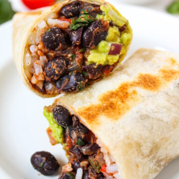 Black bean burrito with rice and guacamole cut in half on a white plate