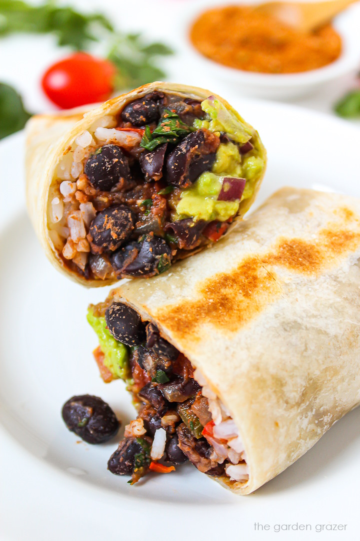 Black bean burrito with rice and guacamole cut in half on a white plate