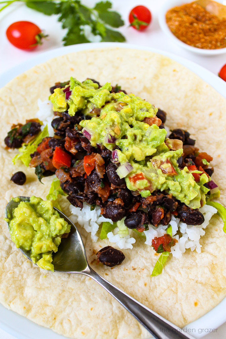 An open-faced bean burrito with rice and guacamole on a white plate
