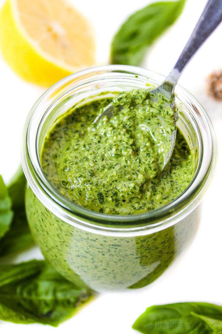 Metal spoon lifting up basil walnut pesto from a small glass jar
