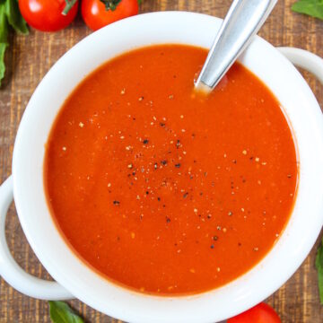 Overhead view of vegan tomato soup in a white serving bowl with spoon