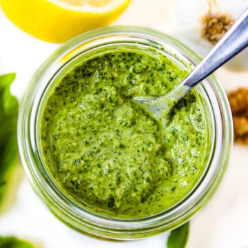 Small glass jar of walnut pesto on a white table with serving spoon