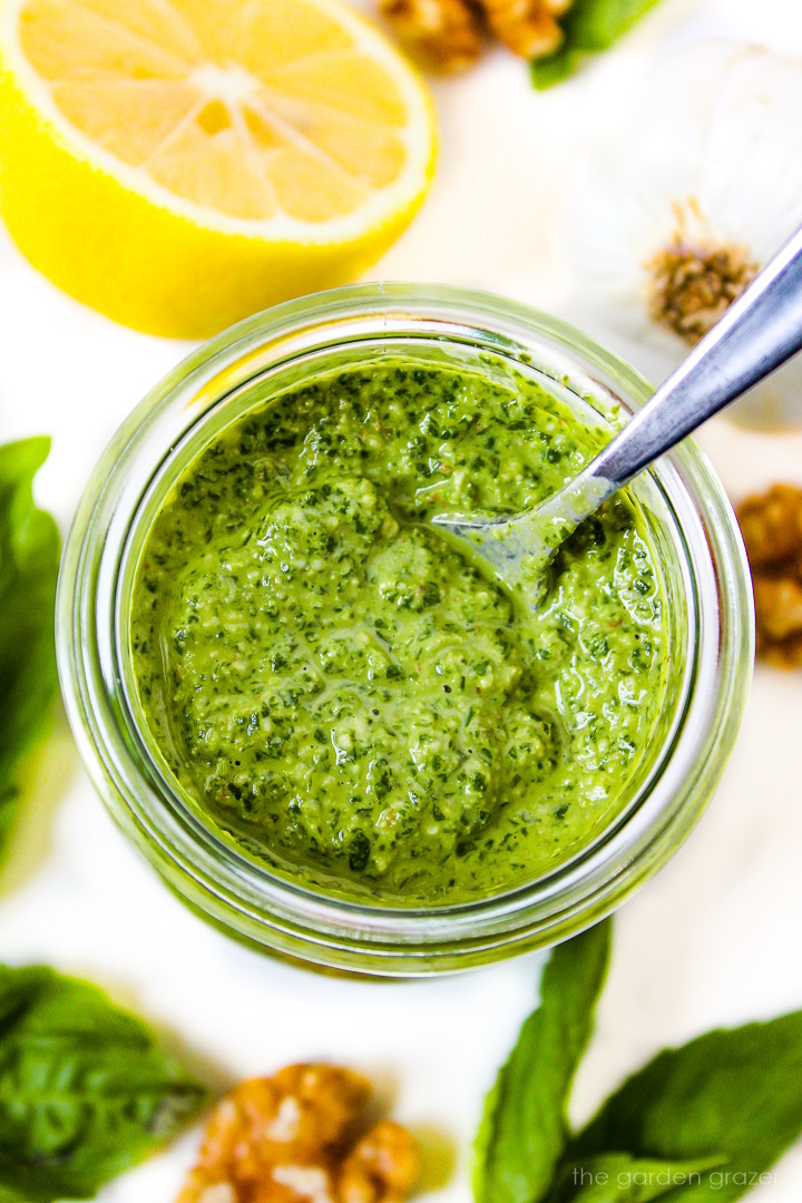 Small glass jar of walnut pesto on a white table with serving spoon