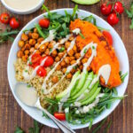 Sweet potato quinoa bowl on a wooden table with tahini dressing and serving spoon