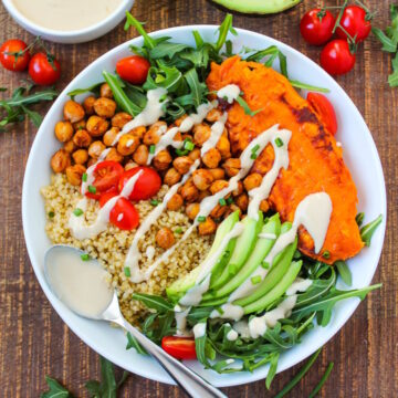 Sweet potato quinoa bowl on a wooden table with tahini dressing and serving spoon