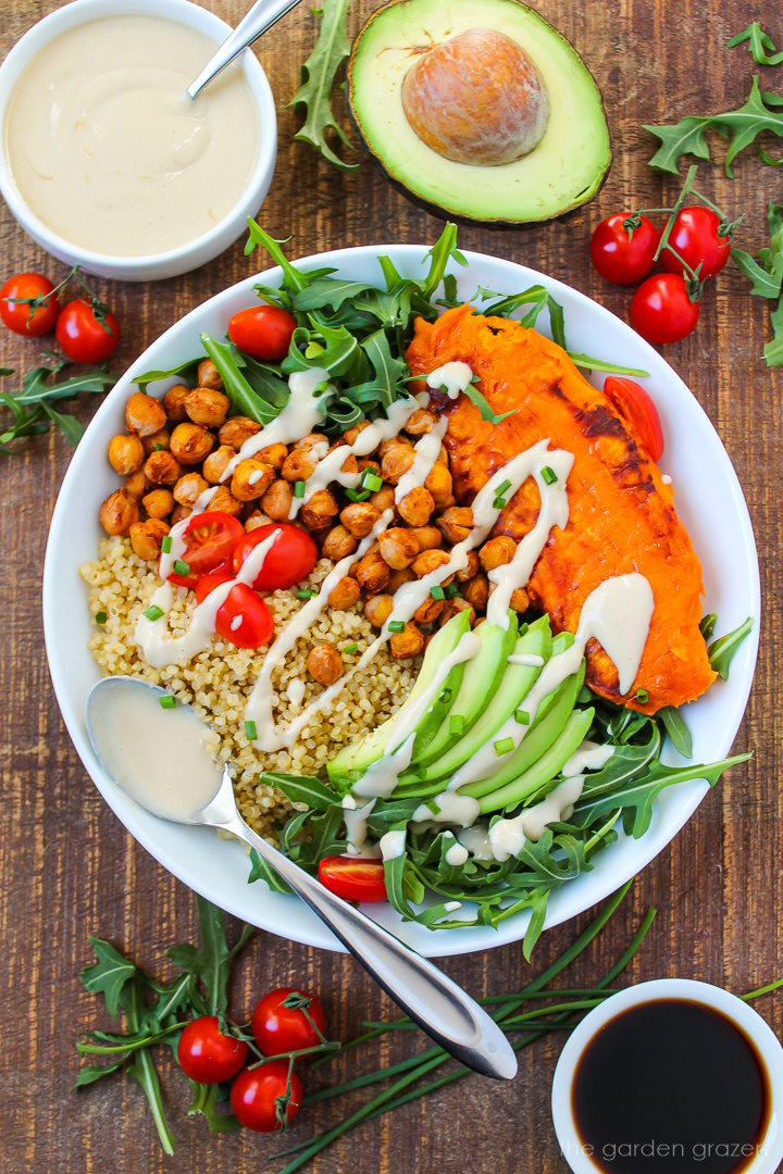 Sweet potato quinoa bowl on a wooden table with tahini dressing and serving spoon