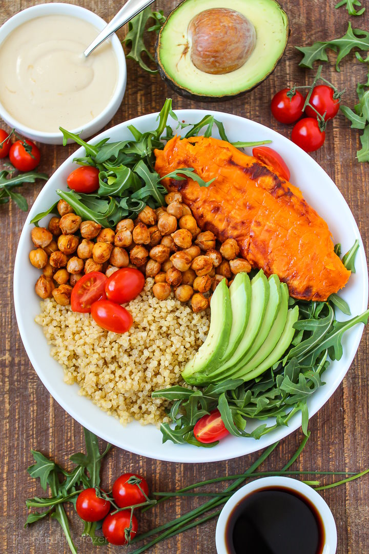 Preparing sweet potato quinoa bowl with sliced avocado, arugula, and tomato