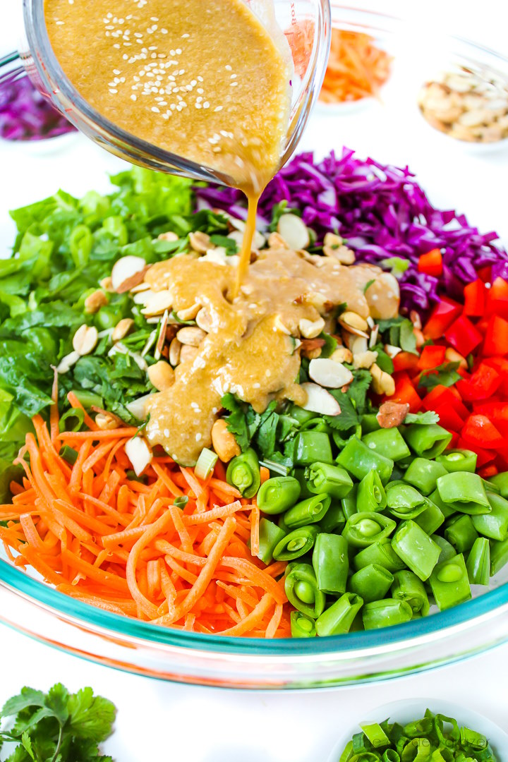 Asian sesame ginger dressing being poured over a chopped salad in a bowl
