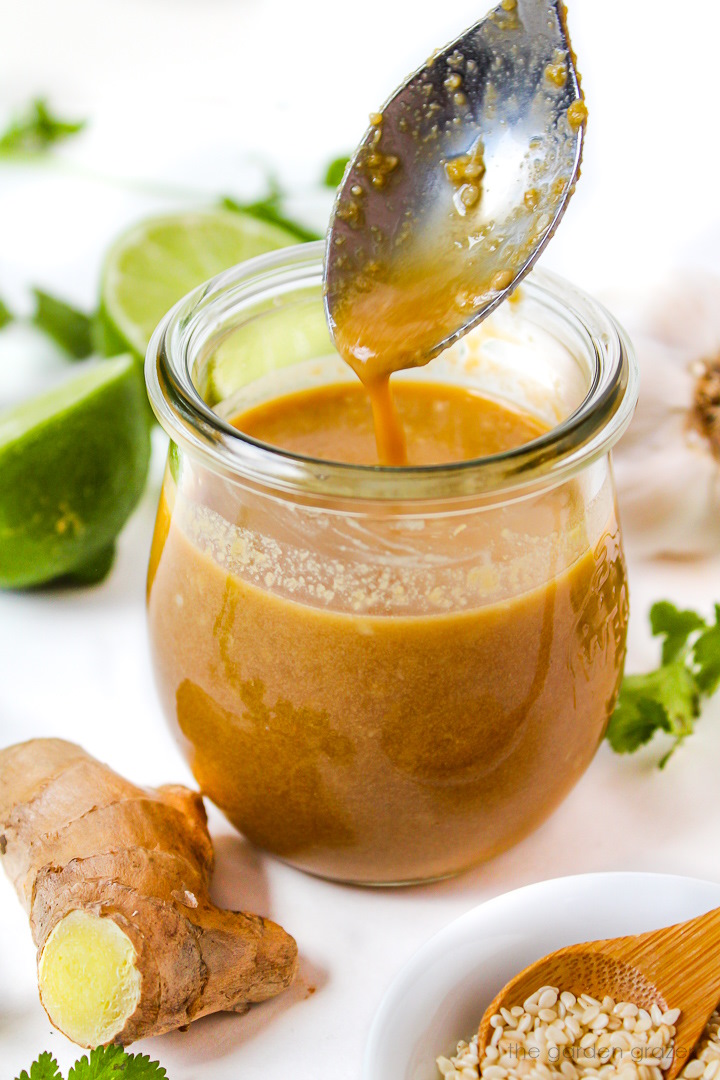 Spoon lifting up Asian sesame ginger dressing from a small glass jar