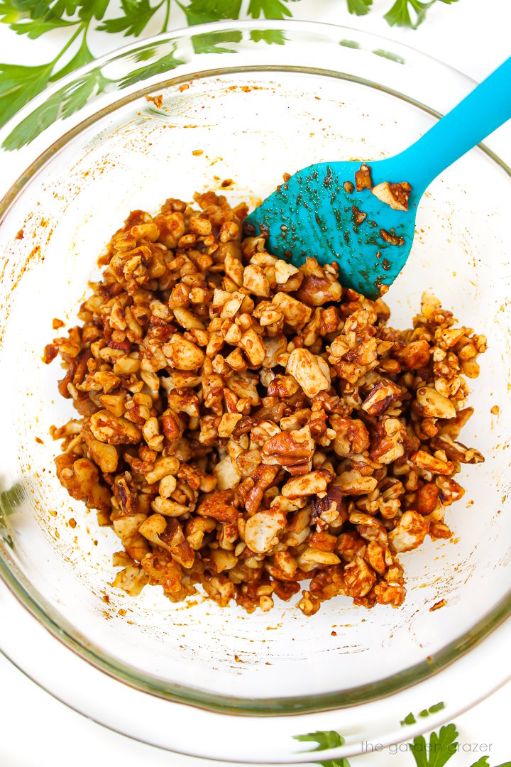 Overhead view of mixing together vegan nut bacon crumbles in a glass bowl before baking