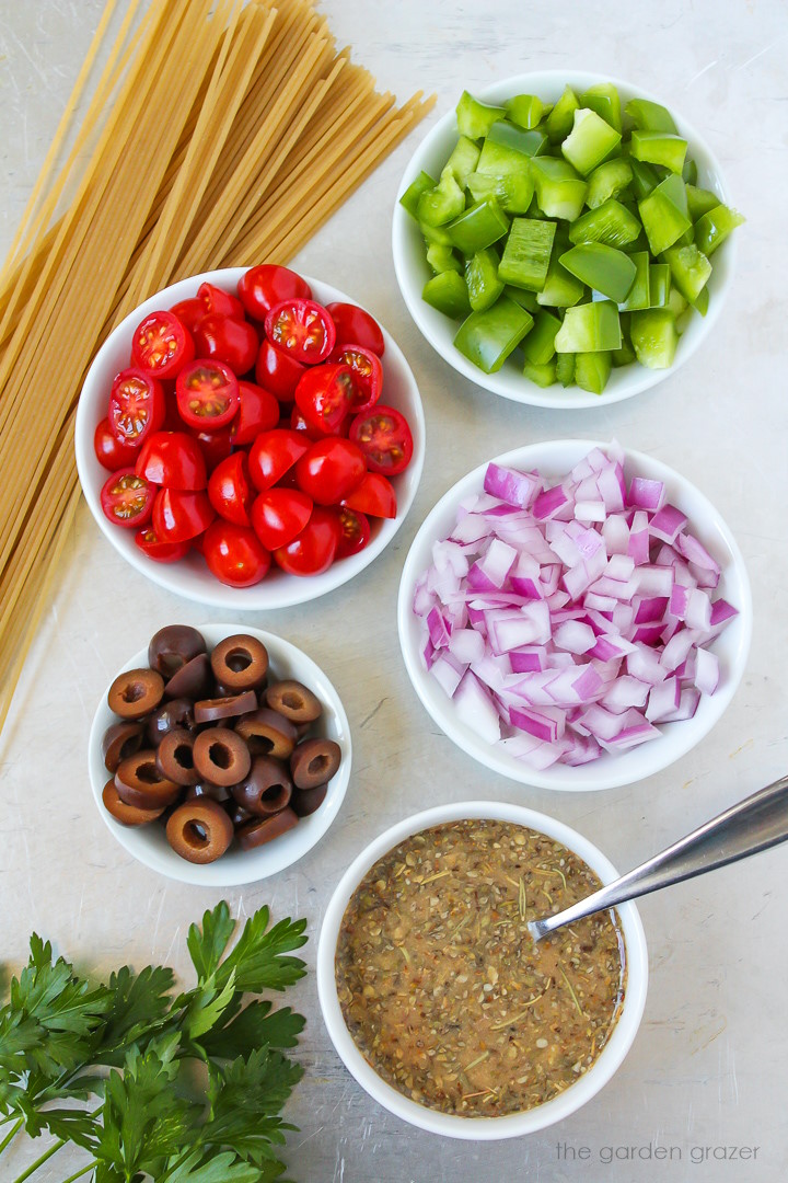 Noodles, tomatoes, bell pepper, onion, olives, and fresh herb ingredients laid out on a metal tray