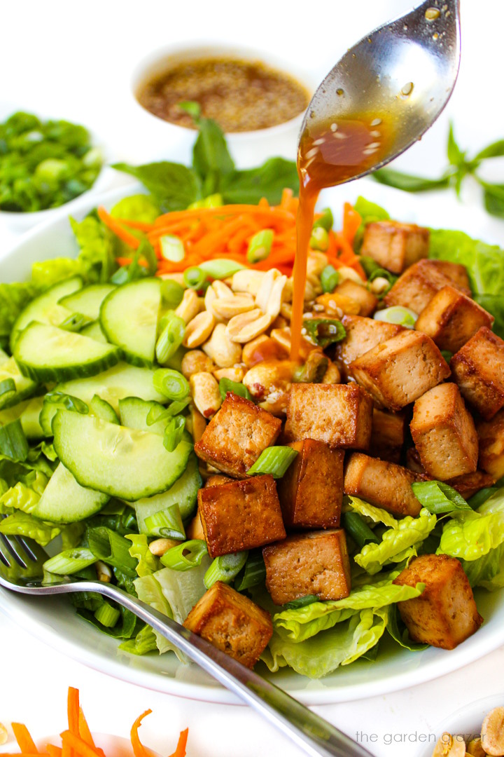 Savory dressing being spooned over Tofu Salad in a white bowl