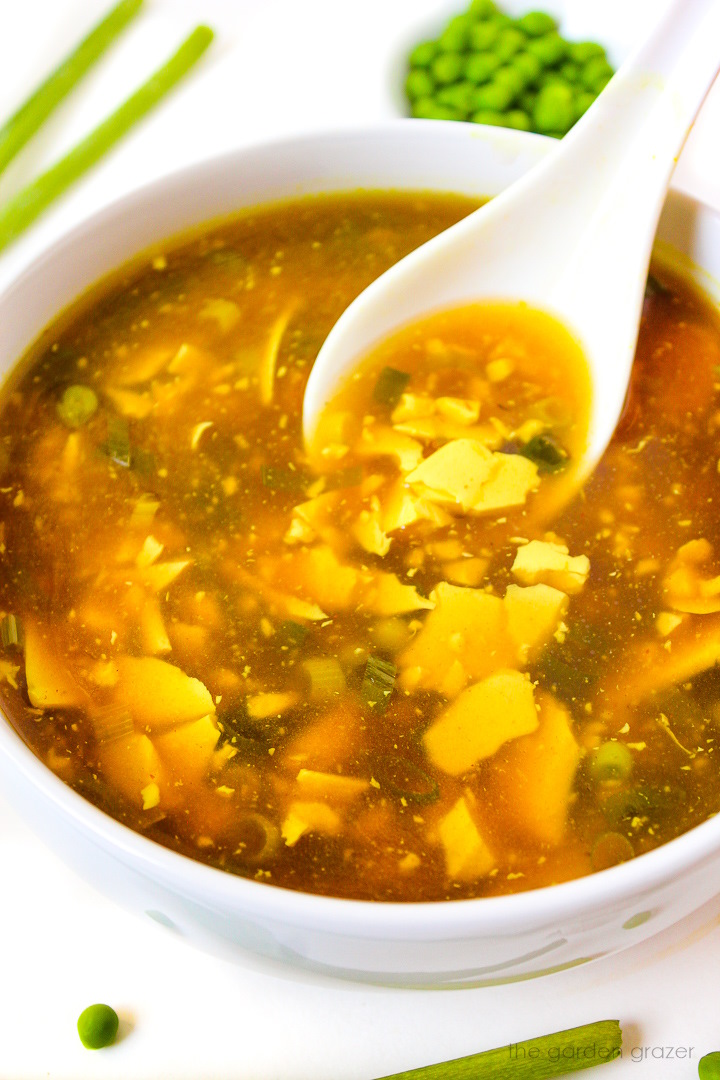 A white serving spoon lifting up vegan egg drop soup from a bowl