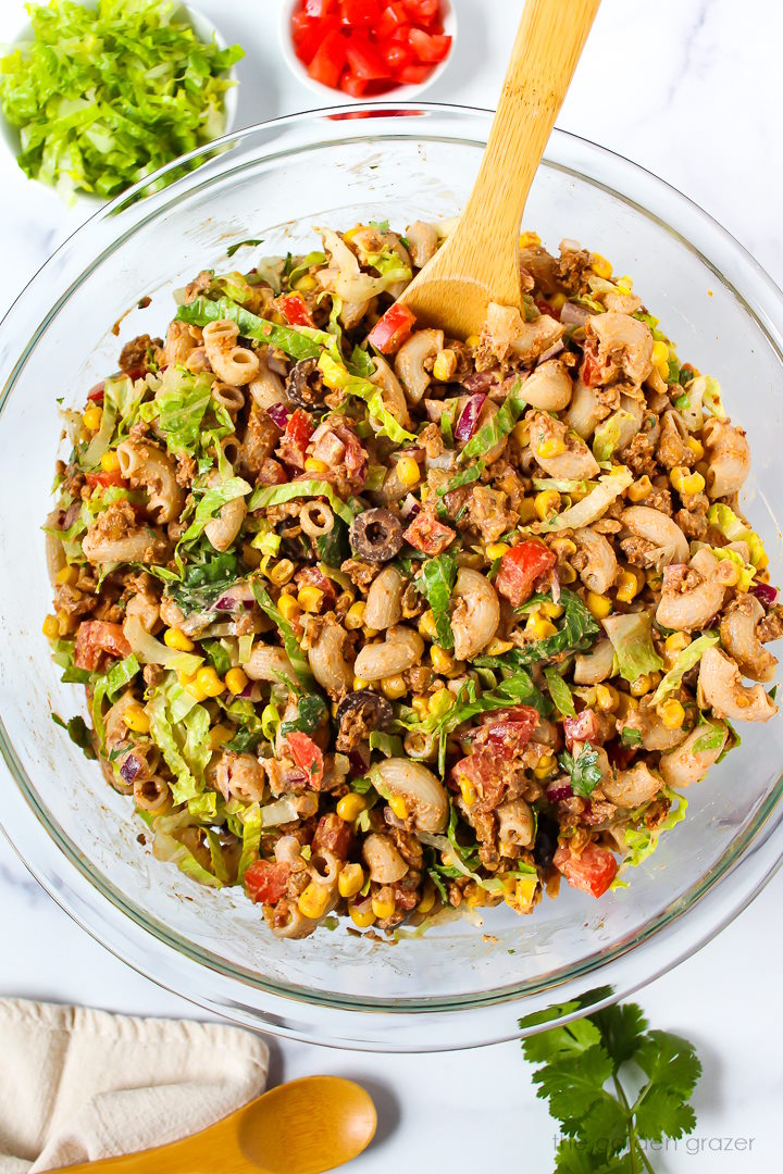 Overhead view of preparing vegan taco pasta salad in a large glass mixing bowl