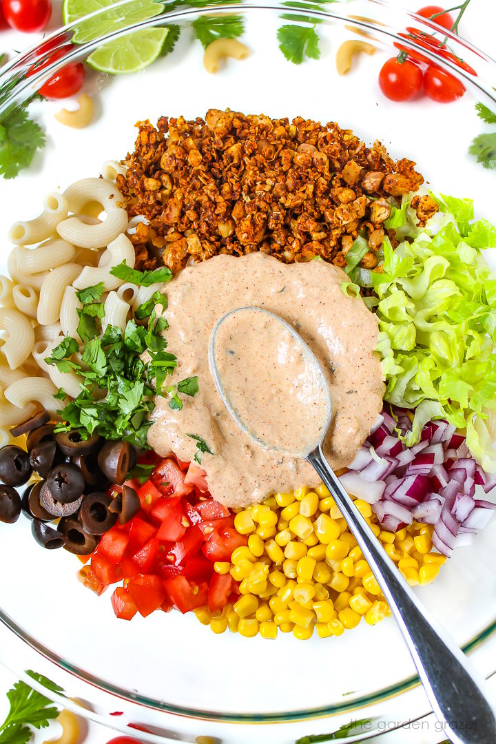 Overhead view of preparing vegan taco pasta salad with dressing in a large glass bowl before mixing together