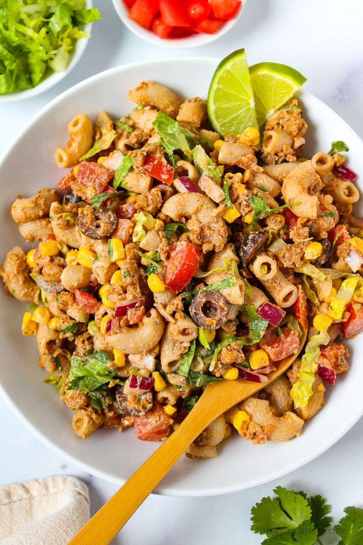 Close up view of vegan taco pasta salad in a white serving bowl with wooden spoon
