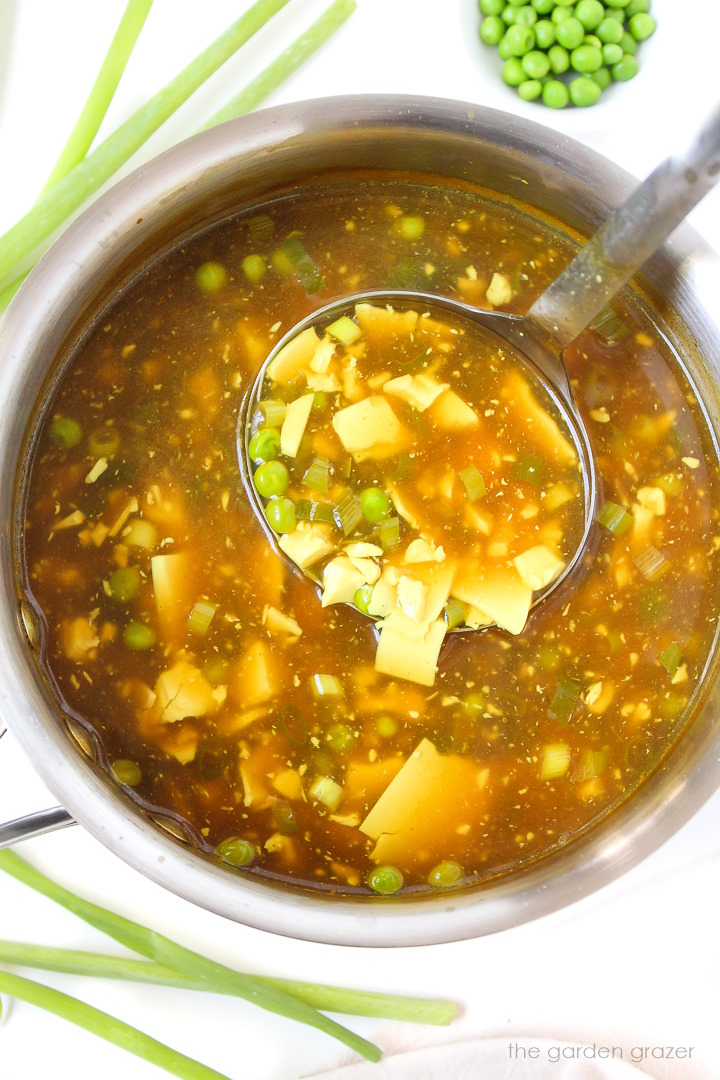 Overhead view of cooking vegan egg drop soup in a medium pot with ladle