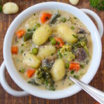 Overhead view of creamy vegan gnocchi soup in a white serving bowl on a wooden table