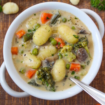 Overhead view of creamy vegan gnocchi soup in a white serving bowl on a wooden table