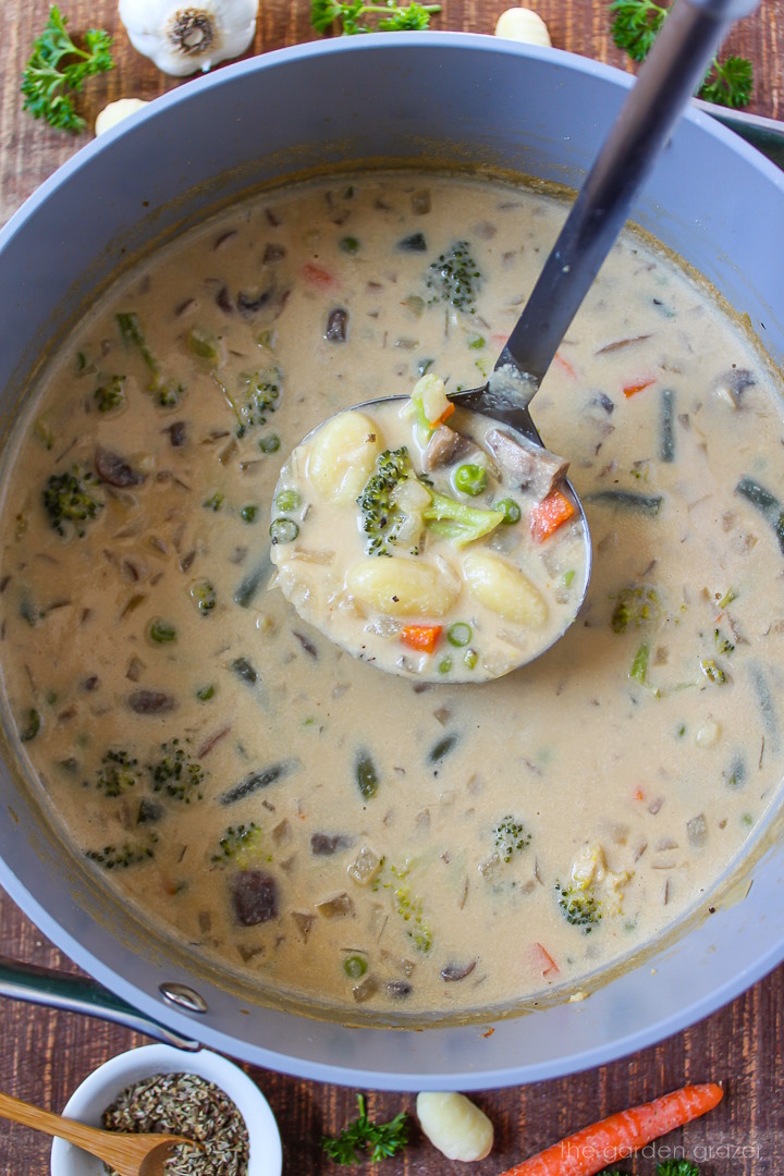 A ladle lifting up vegan creamy gnocchi soup from a large cooking pot
