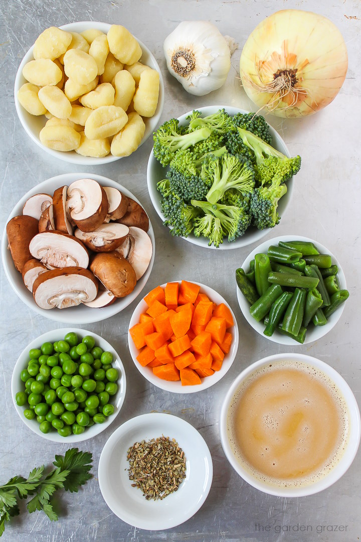 Overhead view of onion, garlic, broccoli, mushrooms, carrot, peas, green beans, and seasoning ingredients laid out on a metal tray