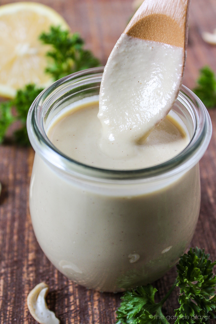 A wooden spoon lifting up cashew alfredo sauce from a small glass jar