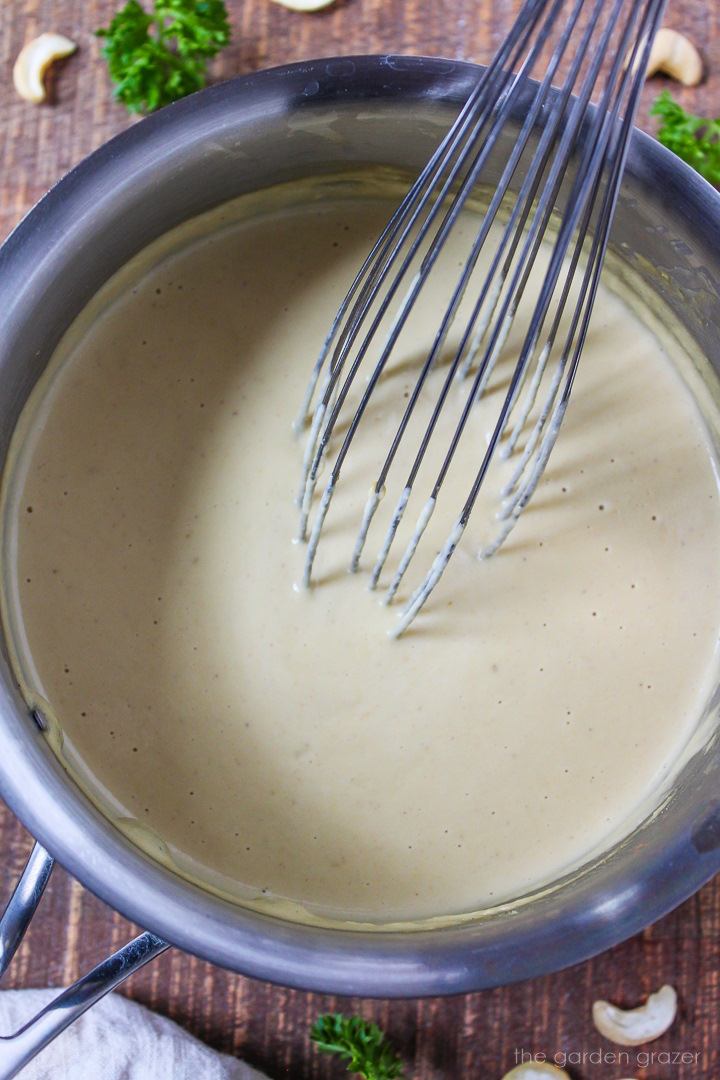 Overhead view of cashew alfredo sauce cooking in a small pot with metal whisk