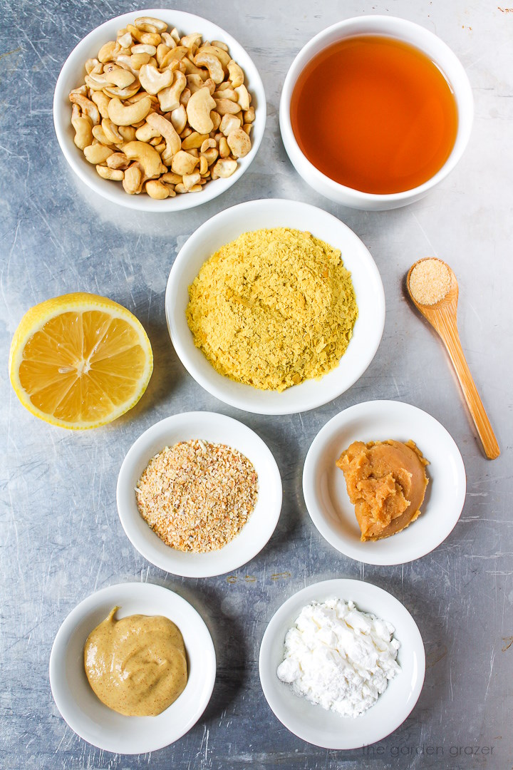 Raw nuts, vegetable broth, nutritional yeast, fresh lemon, miso, and seasoning ingredients laid out on a metal tray