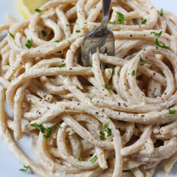 Cashew alfredo sauce tossed with noodles on a white serving plate with fork