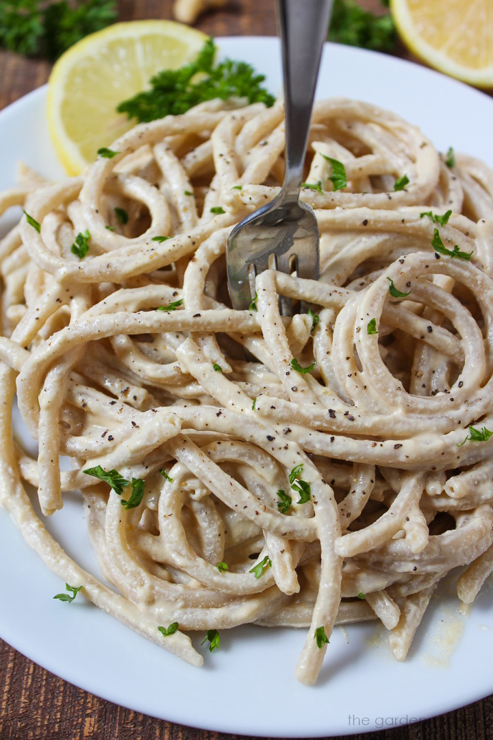 Cashew alfredo sauce tossed with noodles on a white serving plate with fork