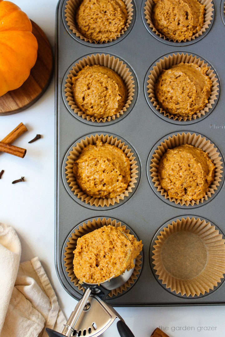 Overhead view of scooping vegan pumpkin muffin batter in a muffin pan before baking