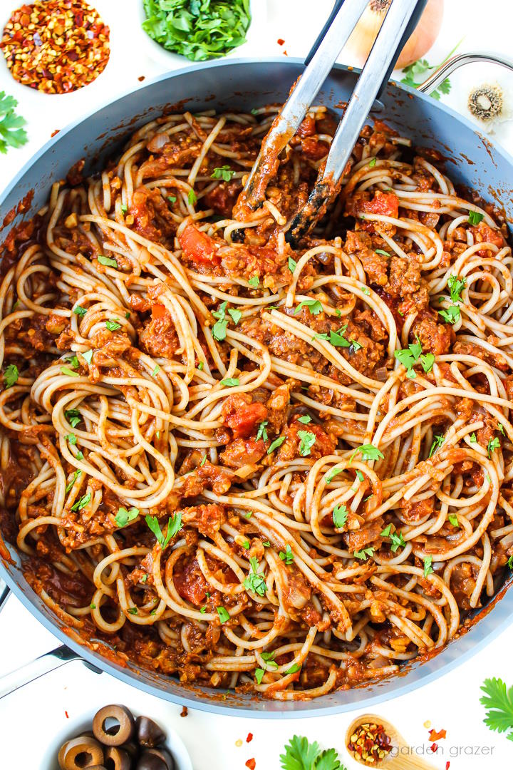Overhead view of taco spaghetti cooking in a large skillet with tongs