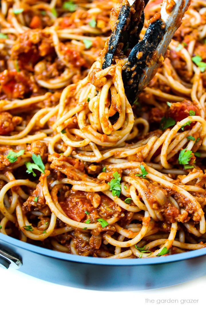 Close up view of tongs lifting some taco spaghetti from a large skillet