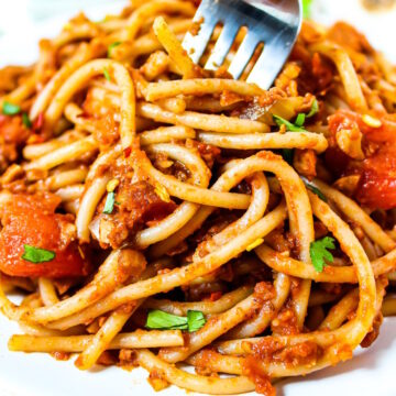 A serving fork lifting up some taco spaghetti from a white plate