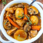 Vegan pot roast in a white serving bowl with spoon on a rustic wooden table