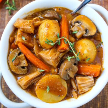 Vegan pot roast in a white serving bowl with spoon on a rustic wooden table