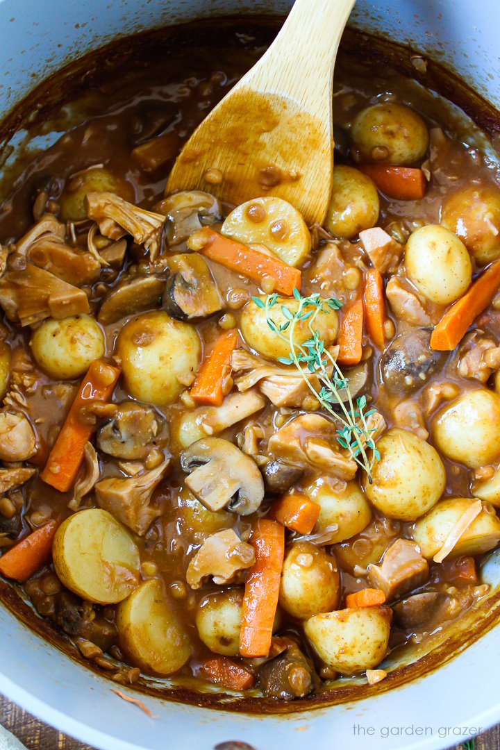 Overhead view of cooked vegan pot roast in a large pot with wooden spoon