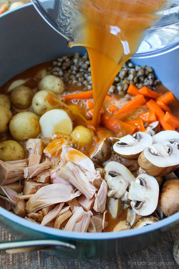 Pouring gravy over vegan pot roast ingredients in a large pot before cooking